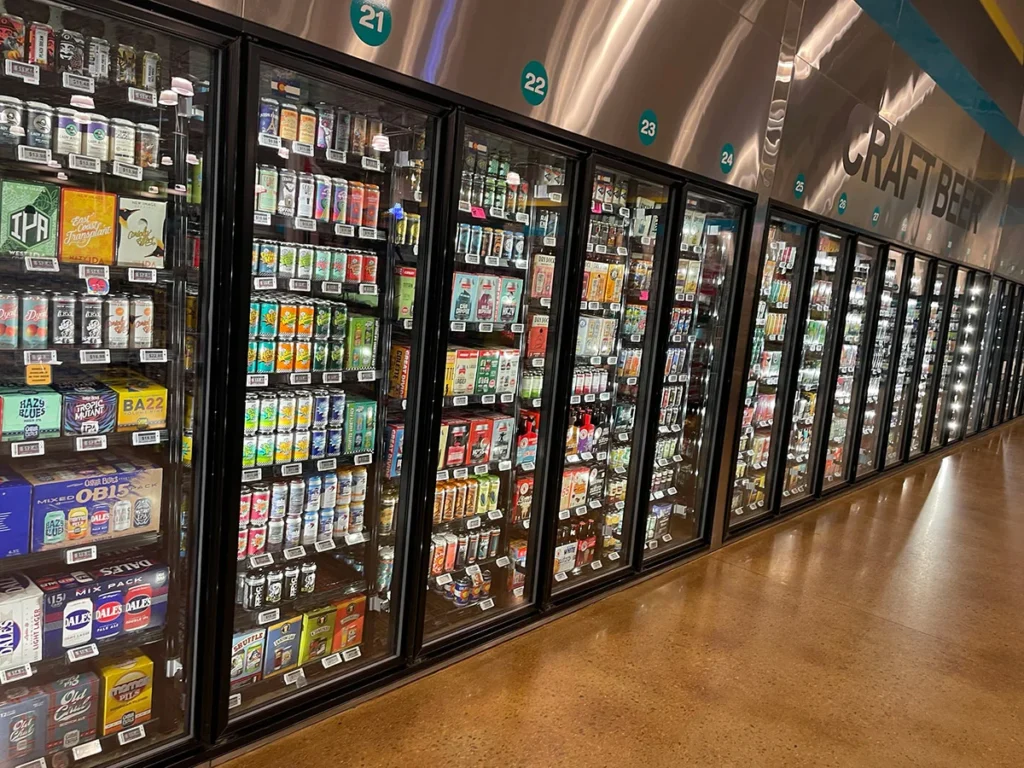 Supermarket craft beer aisle with glass-door refrigerators and assorted beer brands